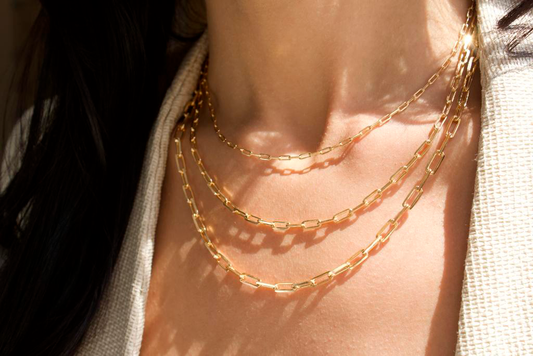 A woman wears three layered gold paperclip link necklaces.