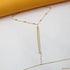 A delicate gold-beaded body chain rests on a clean white surface against an orange backdrop.