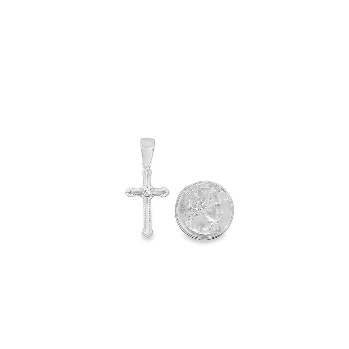 A small white gold cross pendant rests next to a US quarter coin for size comparison.