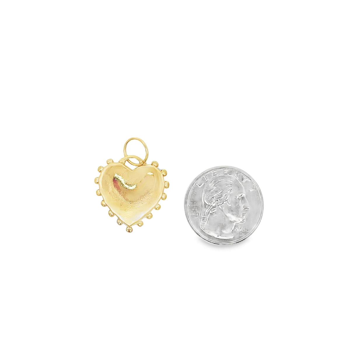 A beaded gold heart charm rests next to a US quarter coin for scale on a white background.
