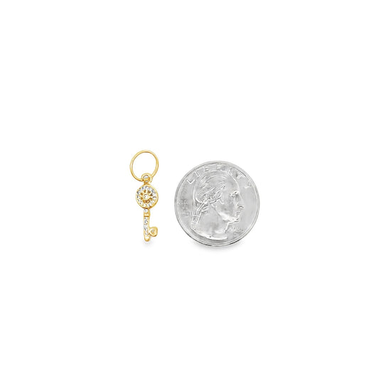 A delicate gold key charm embellished with sparkling diamonds rests next to a US quarter coin to show its compact size.