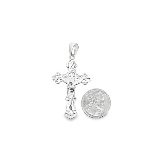 A detailed white gold crucifix pendant rests next to a US quarter coin to showcase its size.