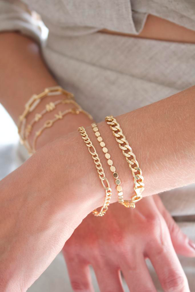 A woman showcases a stylish stack of layered gold bracelets on her wrists.