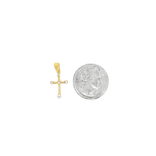 A delicate gold cross pendant featuring sparkling diamond accents rests next to a US quarter for size comparison.