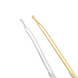 Two delicate layered chain anklets, one in sterling silver and one in gold, rest diagonally against a clean white background.