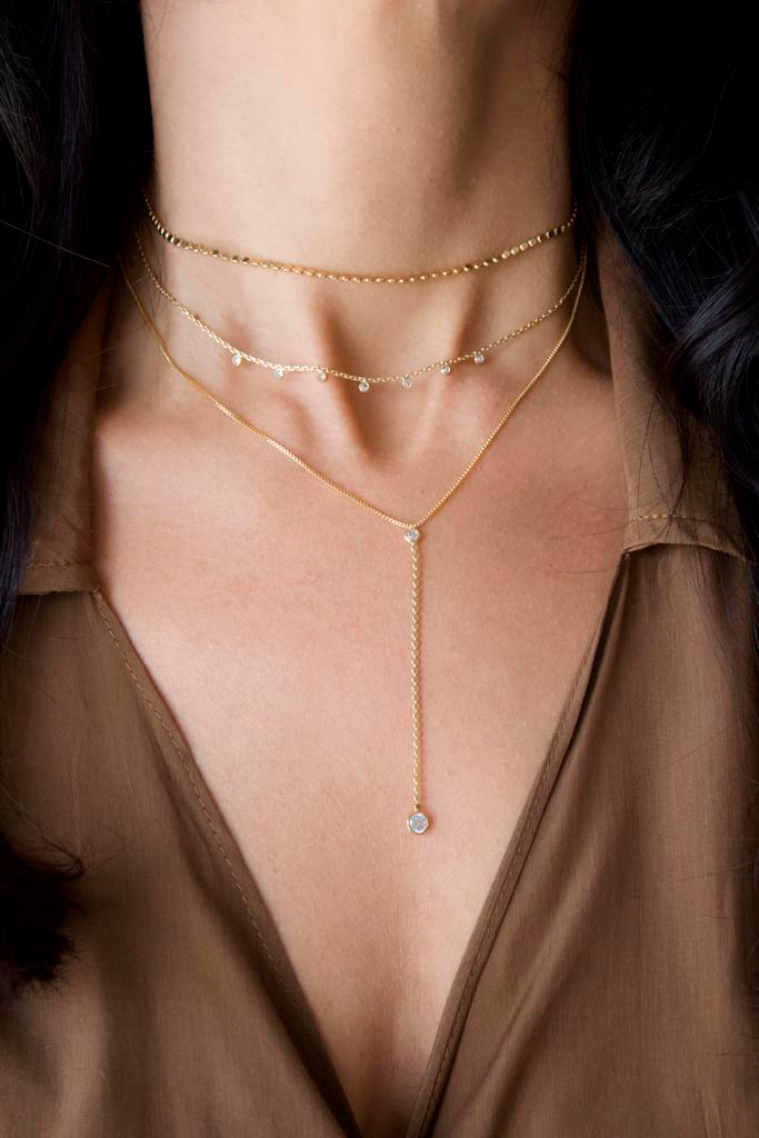 A woman showcases a layered gold necklace set featuring delicate chains, small diamonds, and an elegant lariat design.