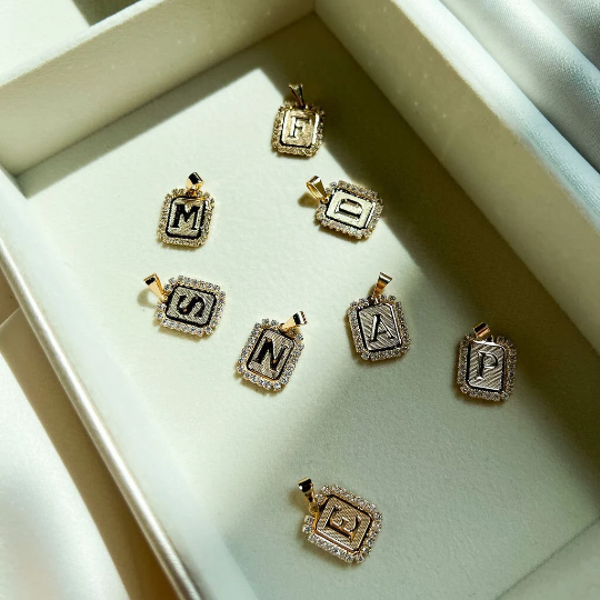 A collection of gold diamond-encrusted initial letter pendants rests neatly inside a white velvet jewelry box.