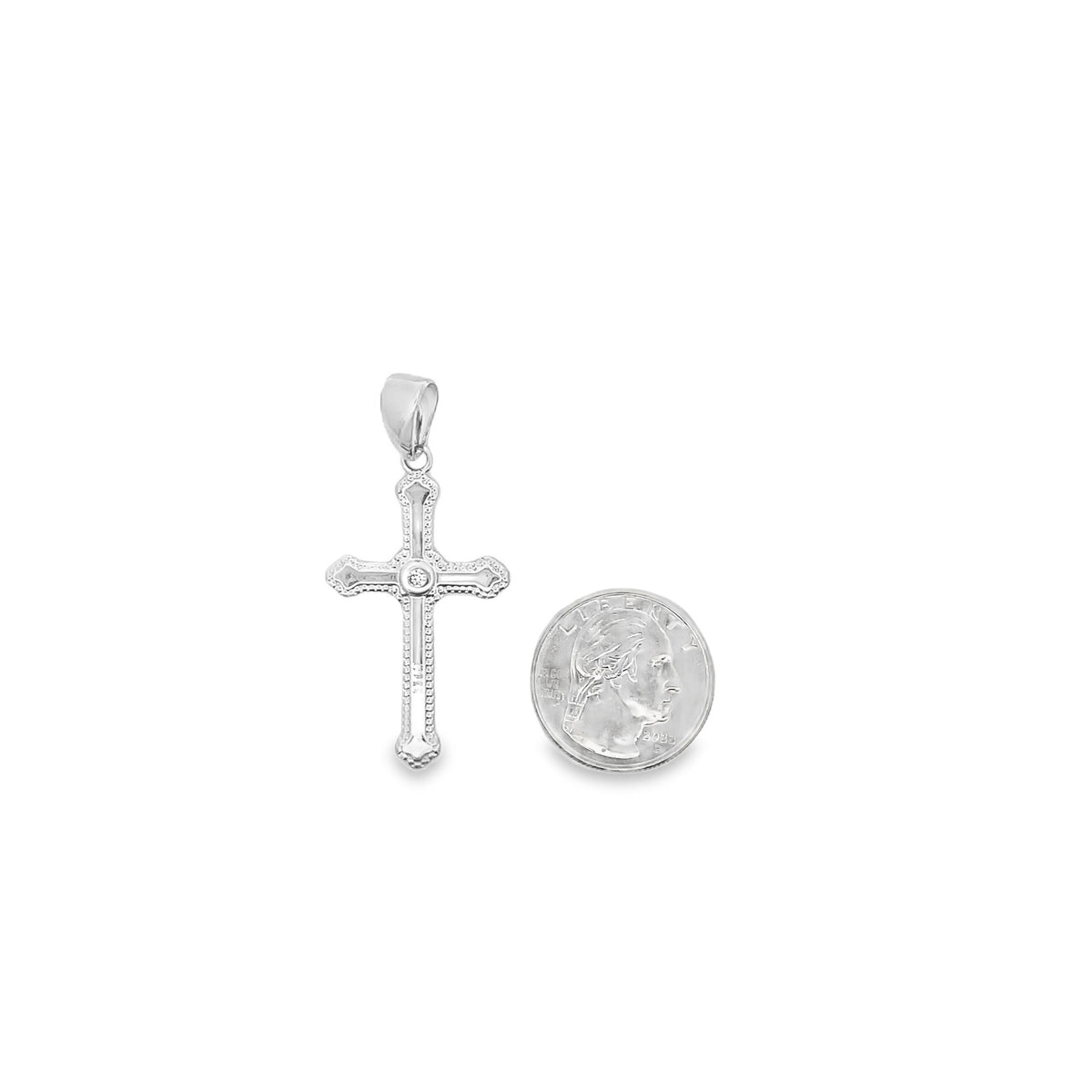 A detailed sterling silver cross pendant with a central diamond accent rests next to a US quarter for size comparison on a clean white background.