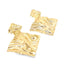 A pair of geometric gold earrings with a rippled, melting texture rests against a white background.