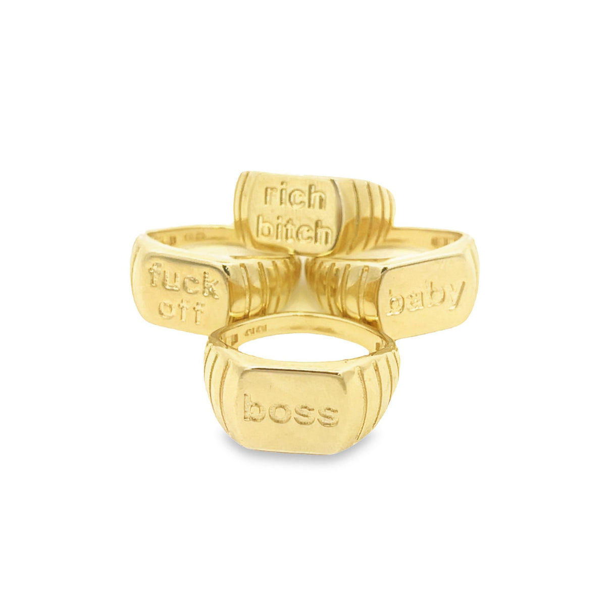 Four gold signet rings engraved with the words "rich bitch," "fuck off," "baby," and "boss" are arranged together on a white background.