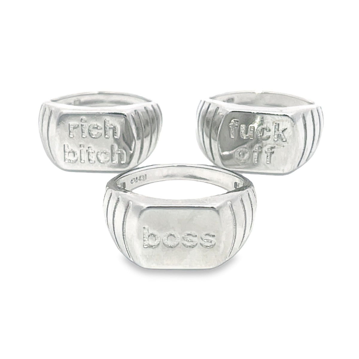 Three chunky sterling silver signet rings display engraved text reading "rich bitch," "fuck off," and "boss."