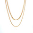 Two delicate gold chain necklaces hang gracefully against a plain white background.