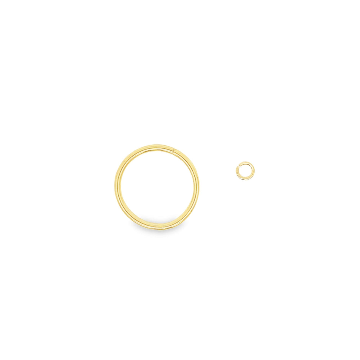 A sleek gold hoop earring lies next to a tiny matching jump ring on a clean white surface.