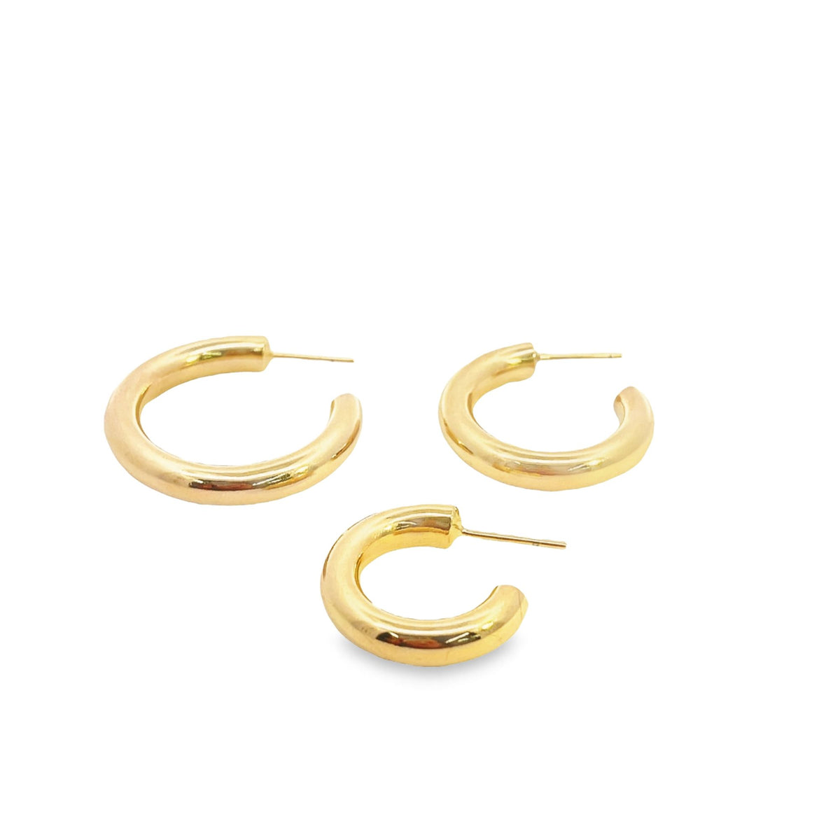 Three thick gold hoop earrings rest on a white surface, showcasing their polished metal finish and sturdy posts.