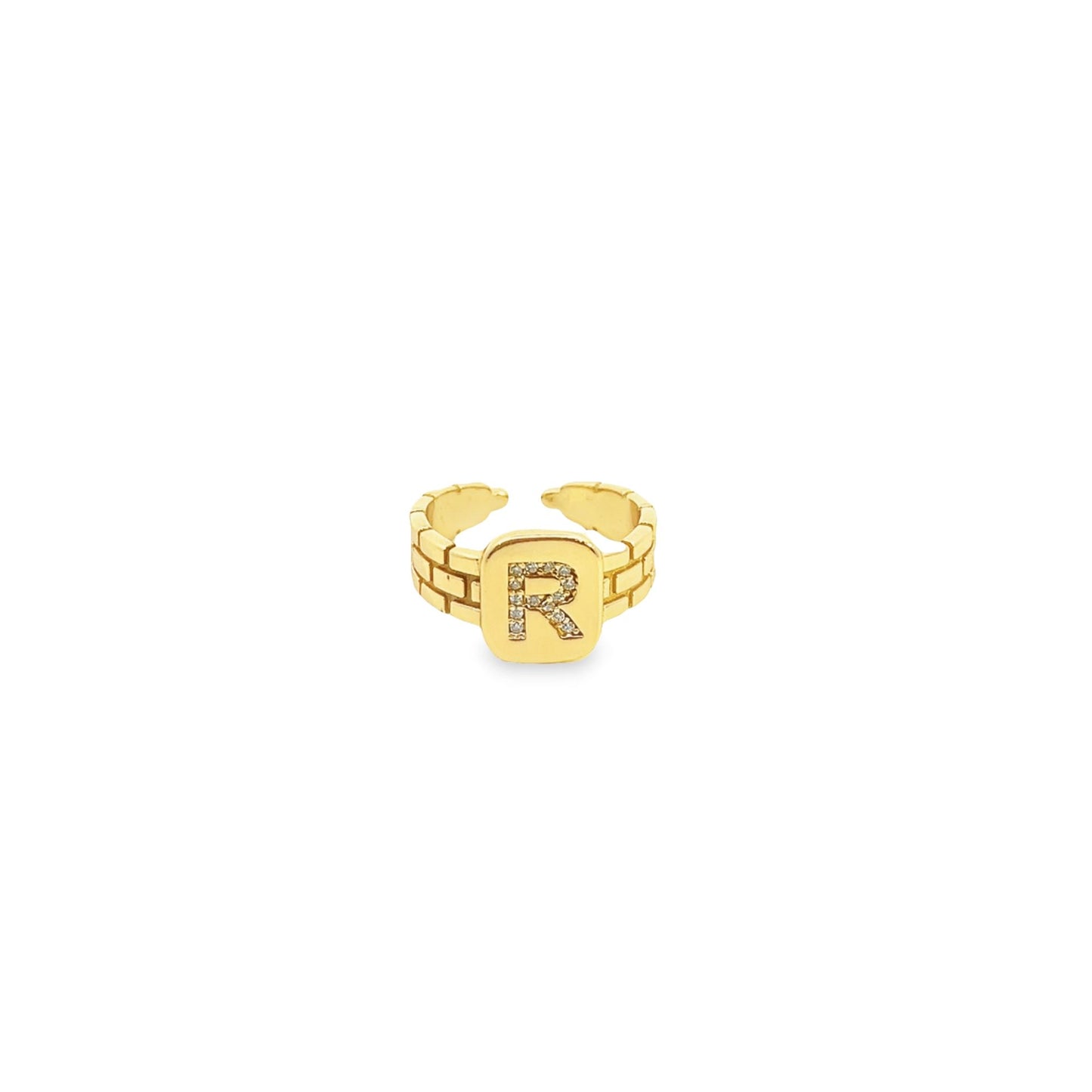 A gold initial R signet ring with a brick pattern band and a pave diamond inlay rests against a clean white background.