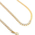 A gold tennis necklace featuring sparkling marquise-cut cubic zirconia stones lies on a clean white surface alongside a smooth gold herringbone chain.