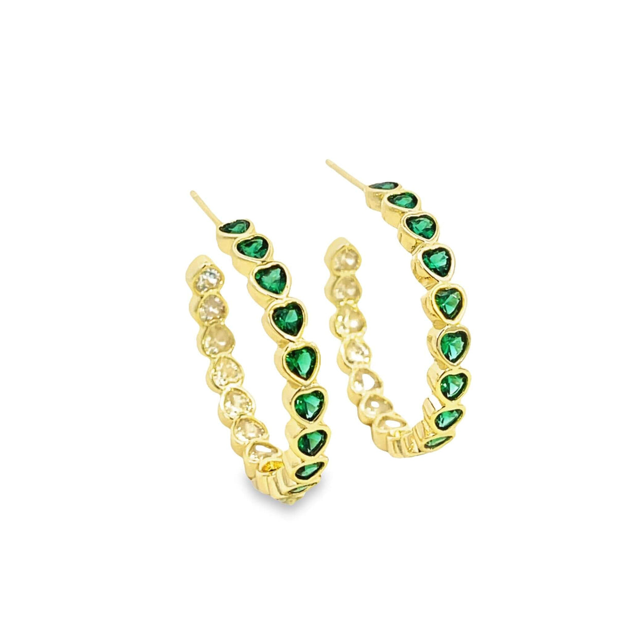 A pair of gold hoop earrings features alternating green and clear heart-shaped cubic zirconia stones set against a clean white background.