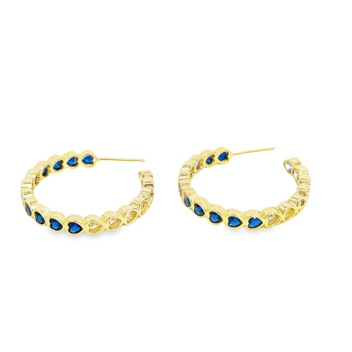A pair of gold hoop earrings features alternating blue and clear heart-shaped crystals on a white background.