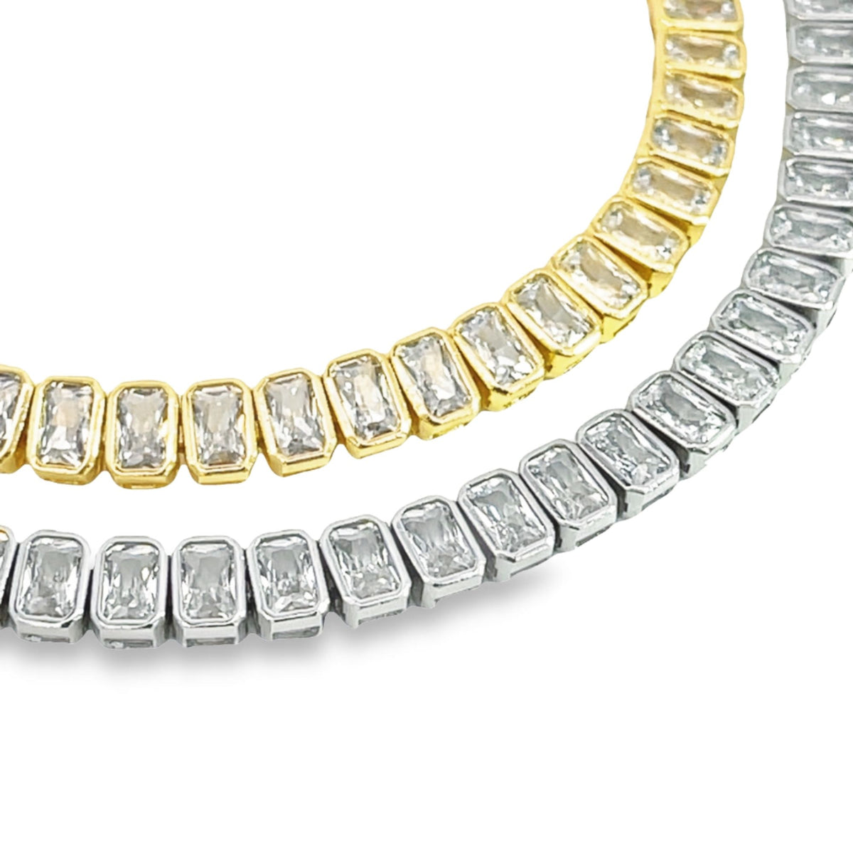 A gold and silver baguette tennis necklace sparkle side-by-side against a white background.