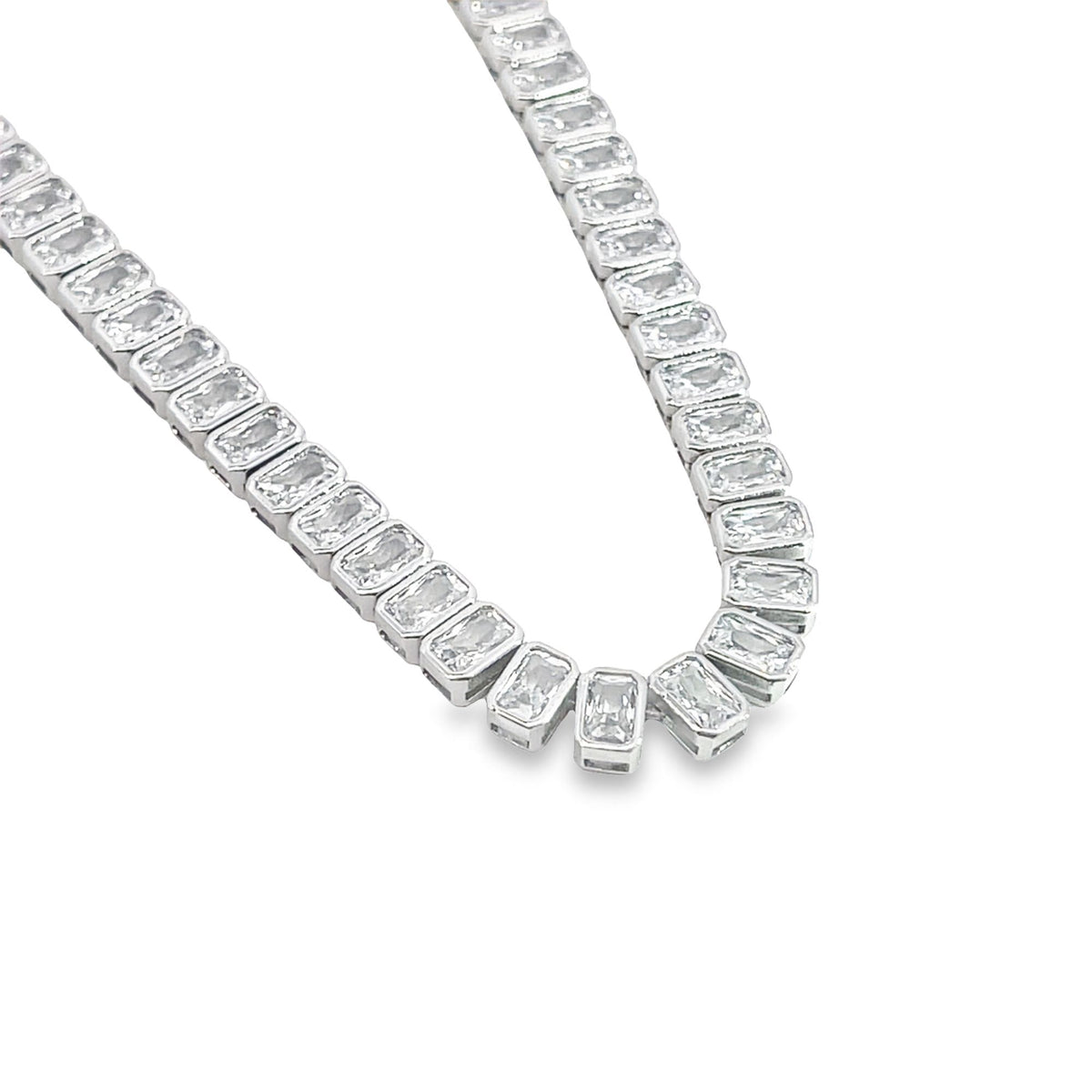 A sparkling diamond tennis necklace featuring emerald-cut stones set in silver curves gracefully against a clean white background.