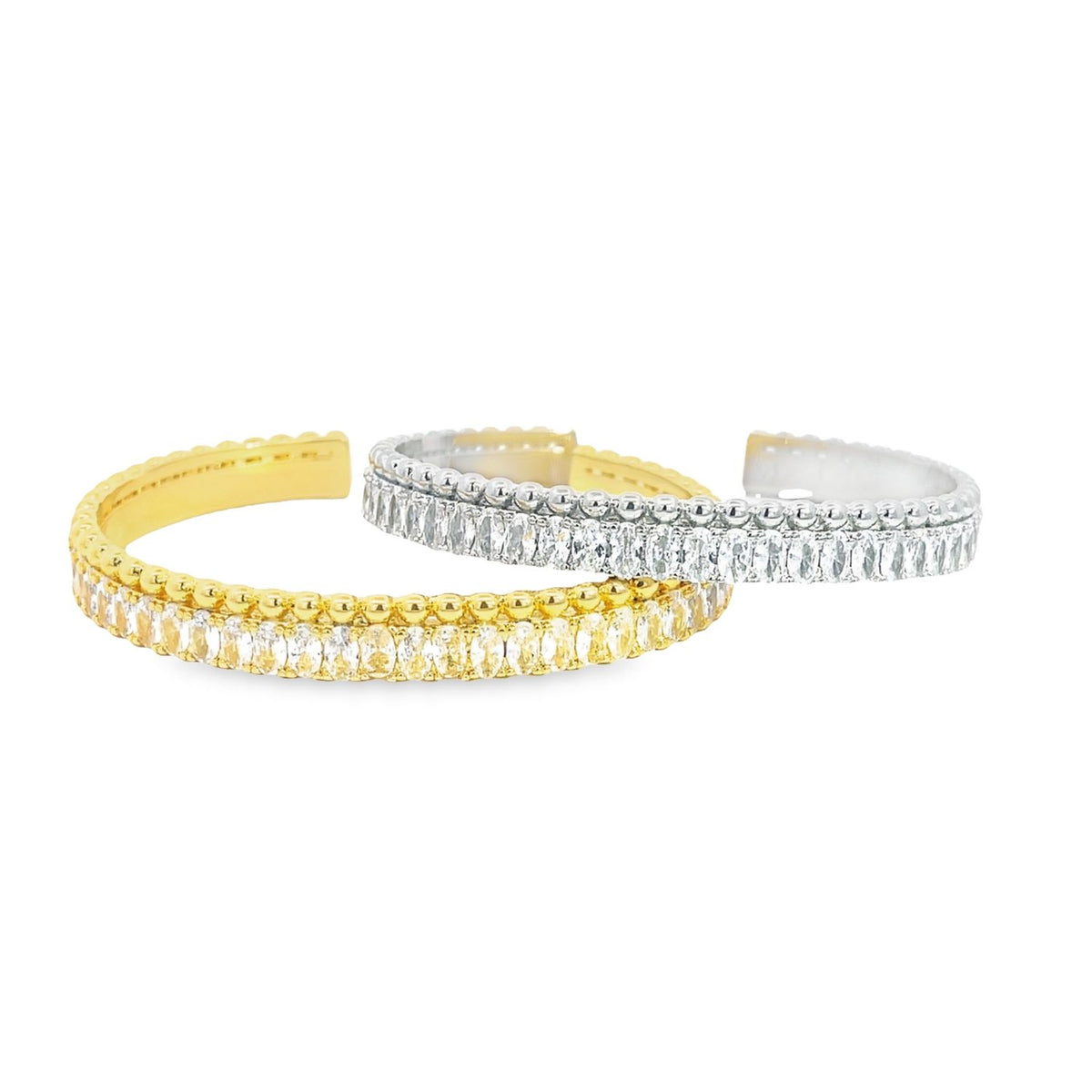 Two elegant diamond cuff bracelets, one in yellow gold and the other in silver, rest side by side against a clean white background.