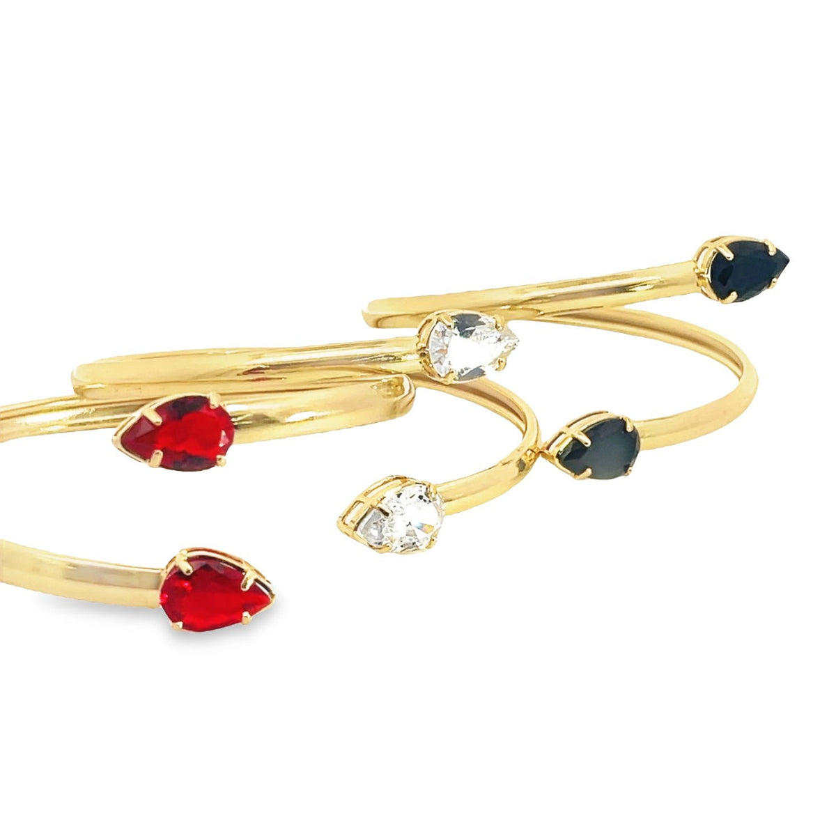 Three gold cuff rings feature dangling teardrop-shaped gemstones in red, white, and black against a white background.