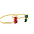 Two gold gemstone bangles, one adorned with square red ruby stones and the other with square green emerald stones, rest side by side against a clean white background.