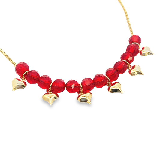 A delicate gold chain necklace features sparkling red crystal beads and dangling gold heart charms against a clean white background.