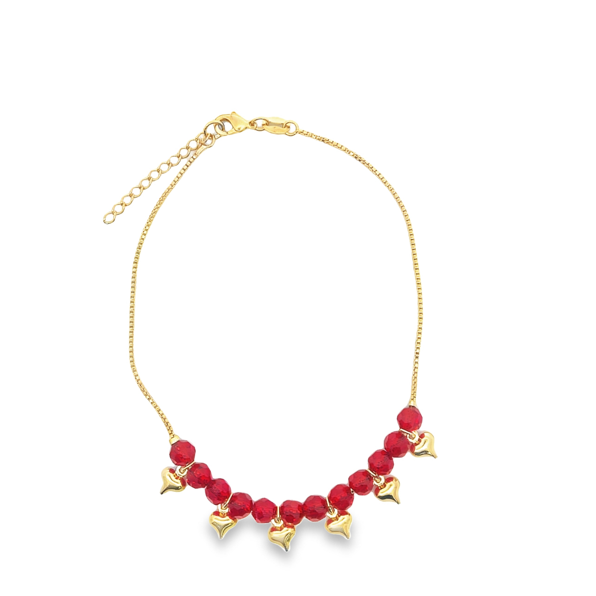 A delicate gold chain necklace sparkles against a plain white background, featuring dangling red crystal beads and tiny gold heart charms.