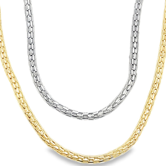 A silver box chain hangs layered above a gold box chain against a white background.