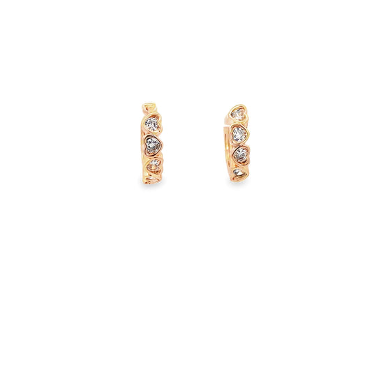 A pair of rose gold huggie hoop earrings featuring sparkling diamond-encrusted heart motifs gleam against a clean white background.
