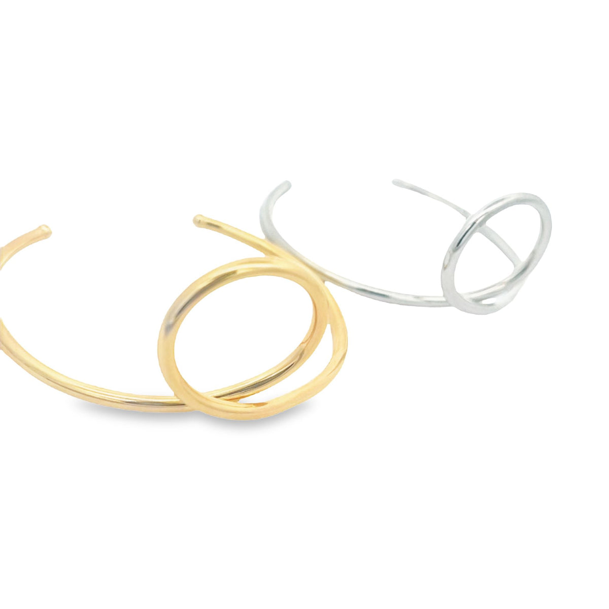 A gold cuff bracelet and a silver cuff bracelet rest side-by-side on a clean white background.