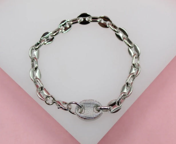 A shiny silver puffed mariner link bracelet rests neatly on a soft white and pink display surface.