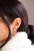 A person models a curated stack of gold earrings, featuring a smooth conch cuff and three graduated ball studs along the earlobe.