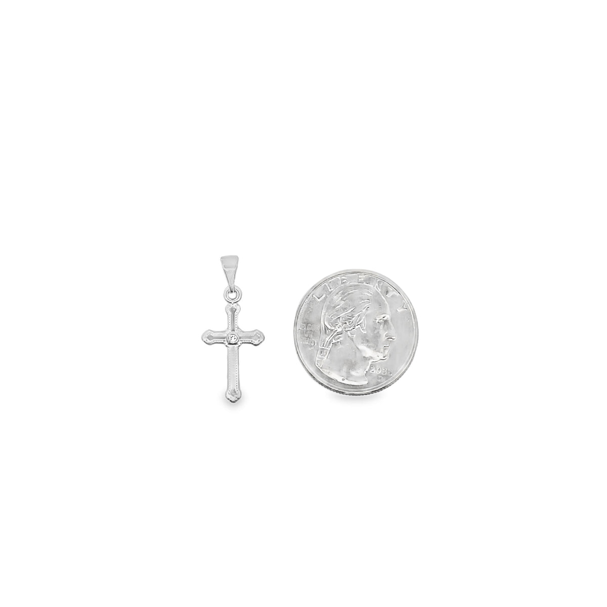 A sterling silver cross pendant featuring a central diamond accent rests next to a US quarter for scale.