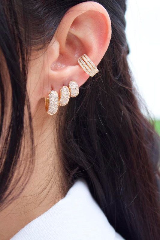 A person wears a dazzling ear stack featuring three graduated diamond-paved gold huggie hoop earrings on the lobe and a matching multi-band ear cuff on the cartilage.