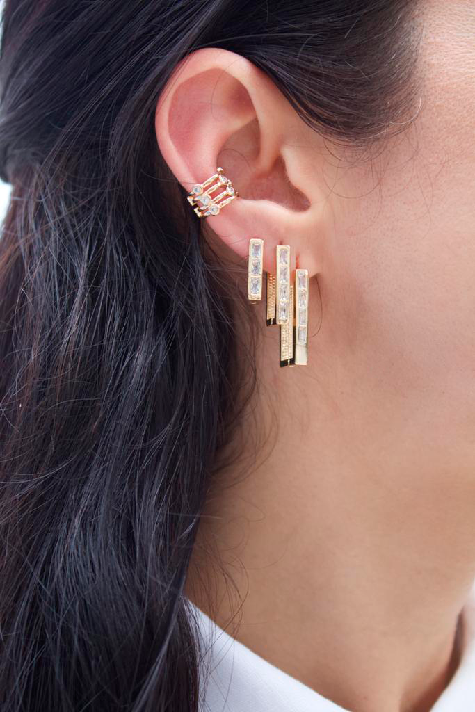 A woman models a trendy gold ear stack featuring a matching multi-bar cuff and dangling rectangular baguette earrings encrusted with sparkling cubic zirconia stones.