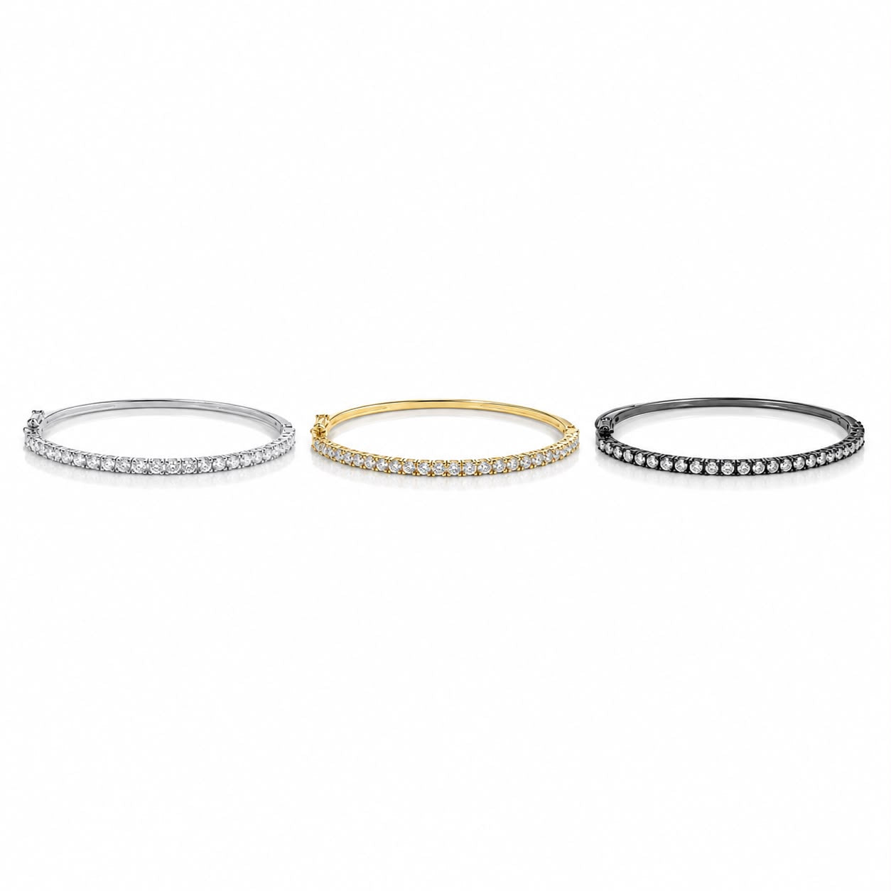 Three elegant diamond tennis bangles in white gold, yellow gold, and black metal rest side by side against a clean white background.
