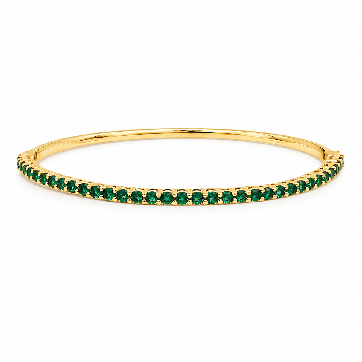 A polished yellow gold bangle bracelet gleams against a white background, featuring a continuous row of vibrant green gemstones set along its front half.
