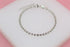 A delicate silver ball chain bracelet rests on a white display surface against a pink background.