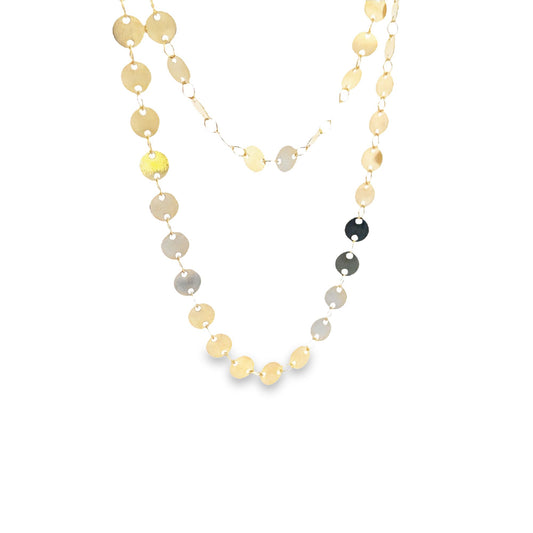 A delicate gold chain necklace drapes against a white background, featuring dangling circular metallic discs that catch the light.
