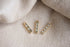Three gold bar earrings accented with sparkling light blue gemstones rest on a textured neutral fabric.