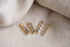 Four gold bar charms featuring bezel-set tanzanite gemstones rest on a textured linen background.