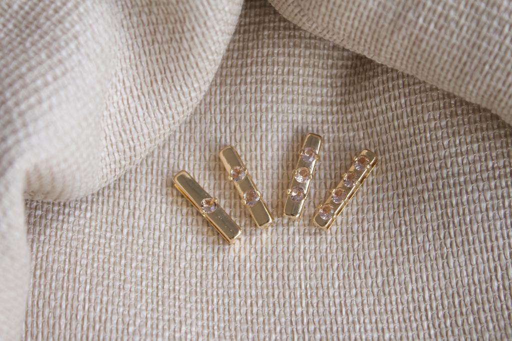 Four gold bar earrings featuring sparkling cubic zirconia stones rest gracefully on textured beige fabric.