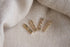 Four gold bar earrings featuring sparkling pink crystals rest on a soft, textured beige fabric.