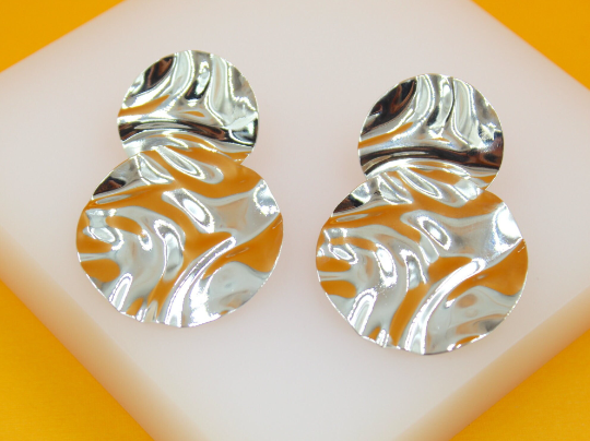 A pair of textured silver drop earrings rest on a white display block.