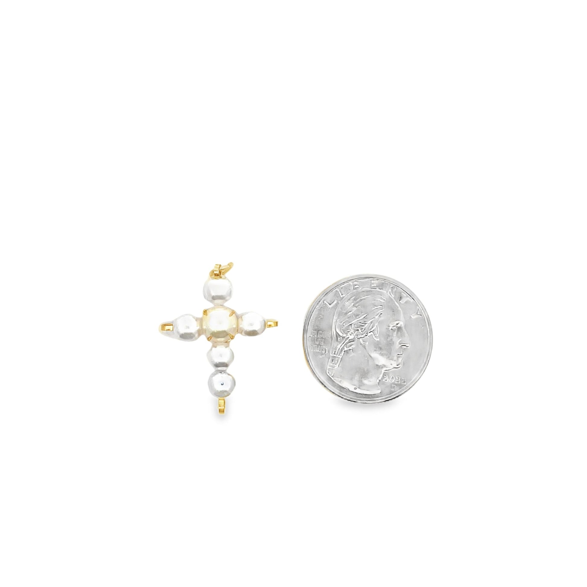 A small pearl cross pendant rests next to a US quarter coin to show scale.