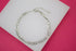 A double-strand silver tennis bracelet featuring interlocking link and crystal-encrusted chains rests on a white display surface against a vibrant pink background.