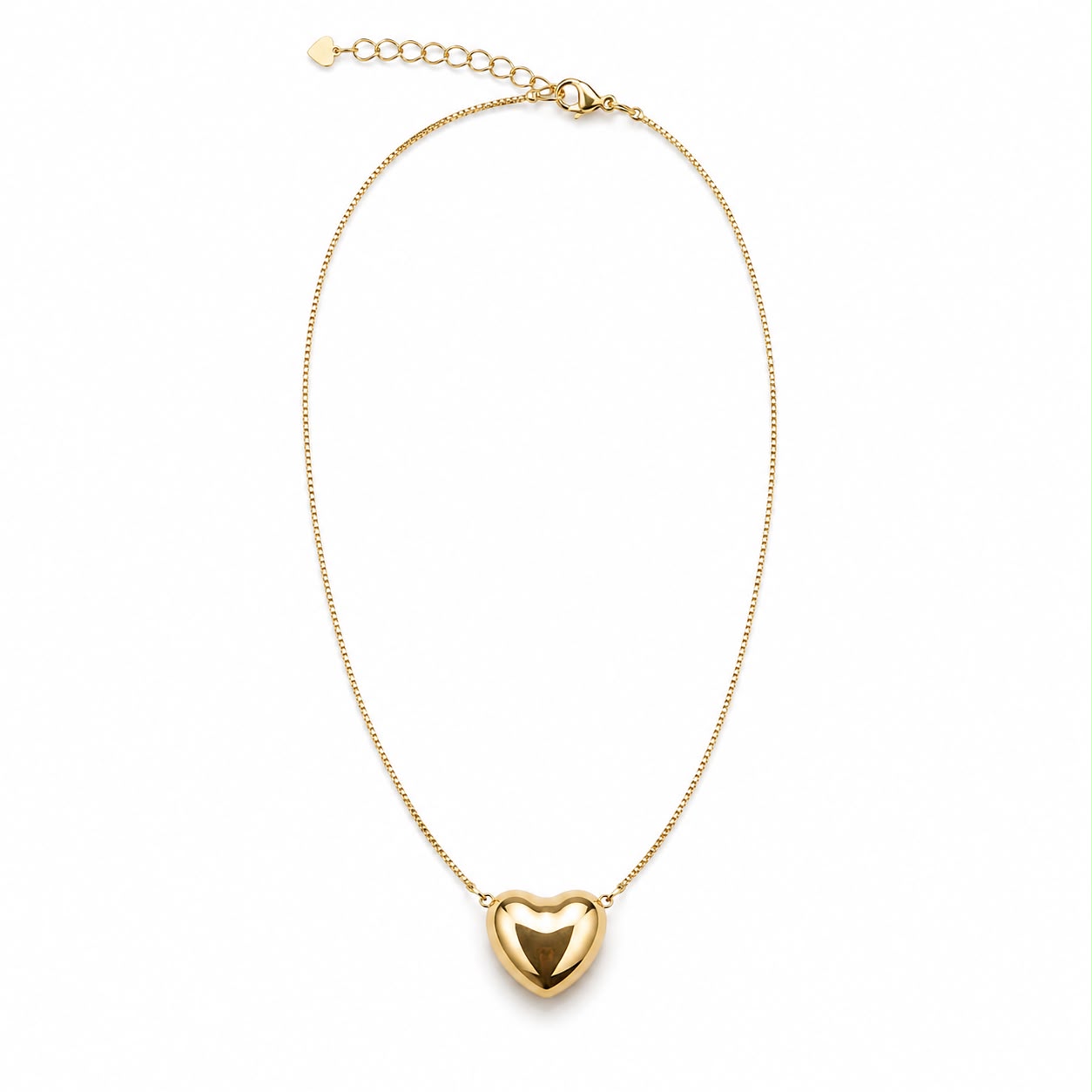 A delicate gold chain necklace hangs against a white background, featuring a polished puffy heart pendant.