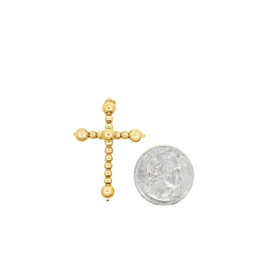 A beaded gold cross pendant rests beside a US quarter to display its size.